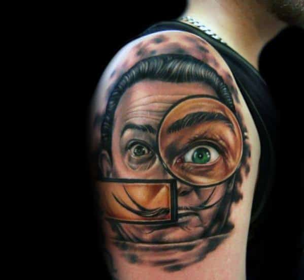 Vivid upper arm tattoo of Salvador Dali with surreal magnified eye, optical distortions, and sharp contrasts capturing his eccentric persona.