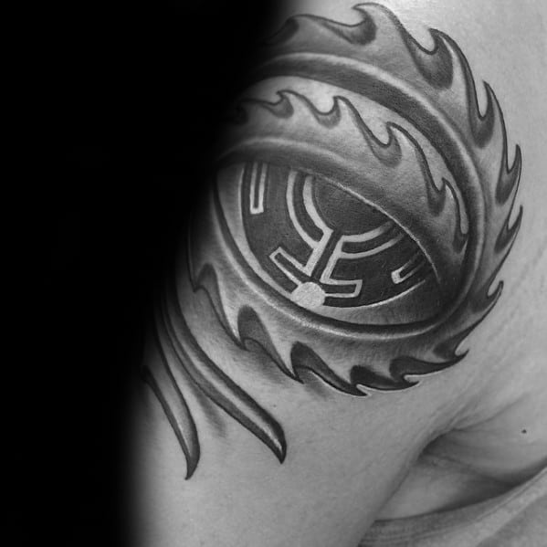 Black and grey Tool-inspired upper arm tattoo of a bold flaming eye with a stylized, maze-like iris design and sharp, curved flame accents.