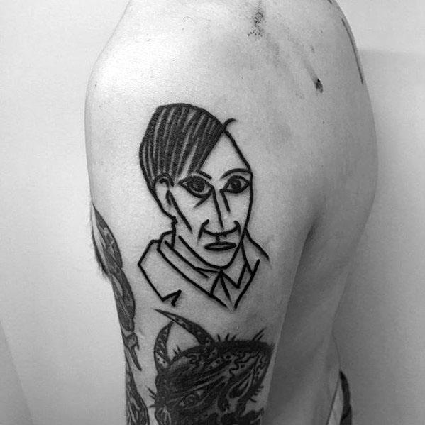 Simple black line tattoo of Pablo Picasso’s portrait, drawn in a bold and abstract style on the upper arm.