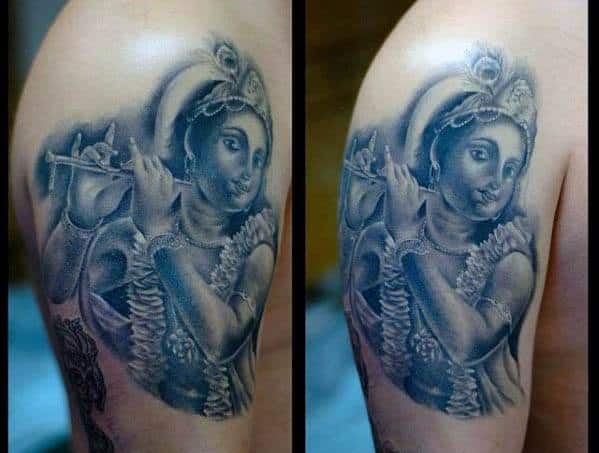 Shaded upper arm tattoo of young Krishna playing the flute, featuring soft facial details, floral garlands, and gentle divine expression.