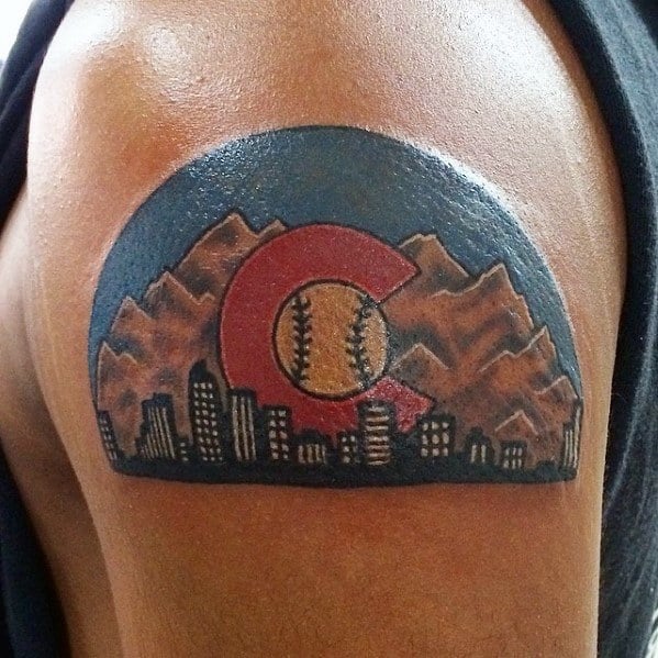 Colorful upper arm tattoo of Denver skyline with mountains, Colorado “C,” and a baseball at the center, symbolizing city and sport pride.