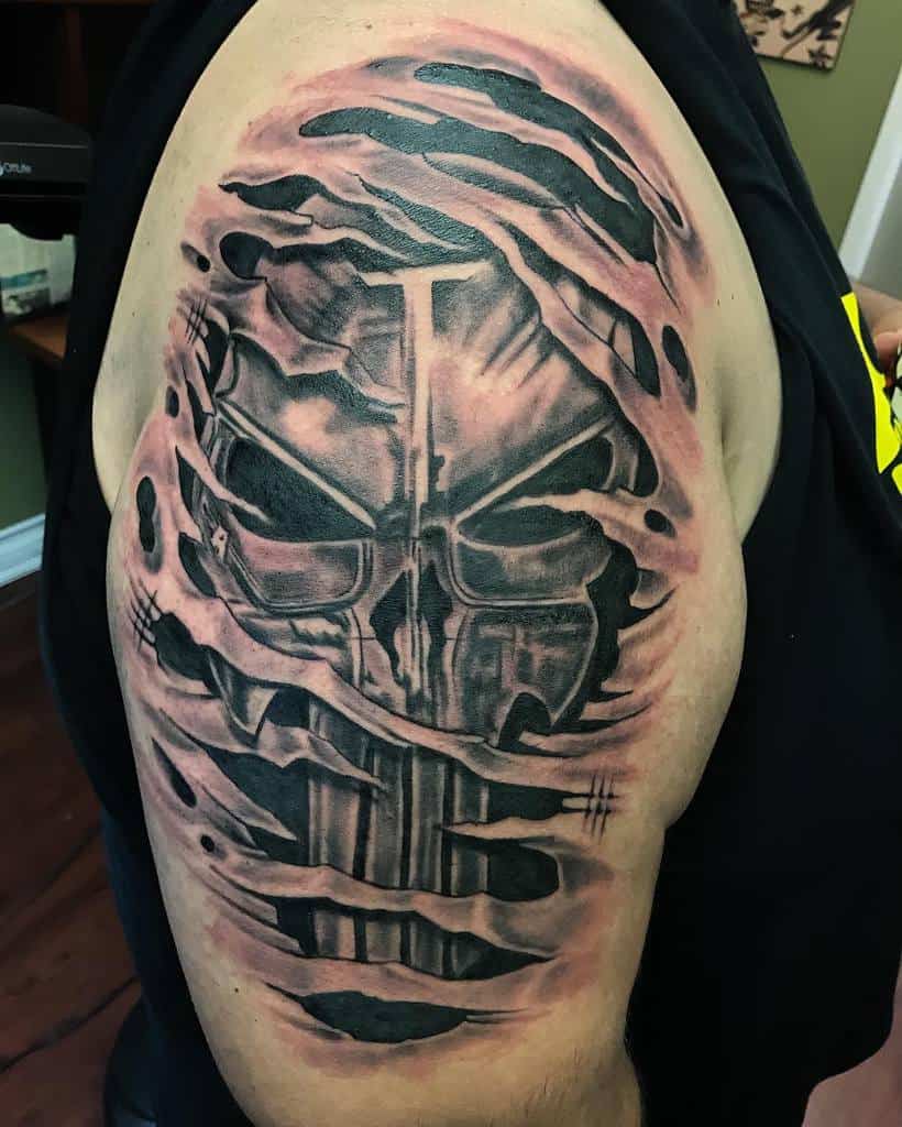 Upper arm tattoo of a Punisher Skull with a shredded skin effect, showing the skull appearing through torn skin