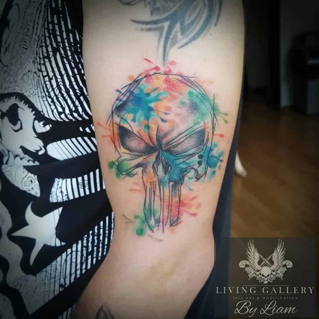 Tattoo of a colorful, watercolor-style Punisher Skull on an upper arm