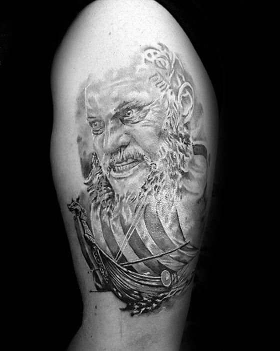 Black-and-gray tattoo of Ragnar Lothbrok with an intense expression and a Viking longship.