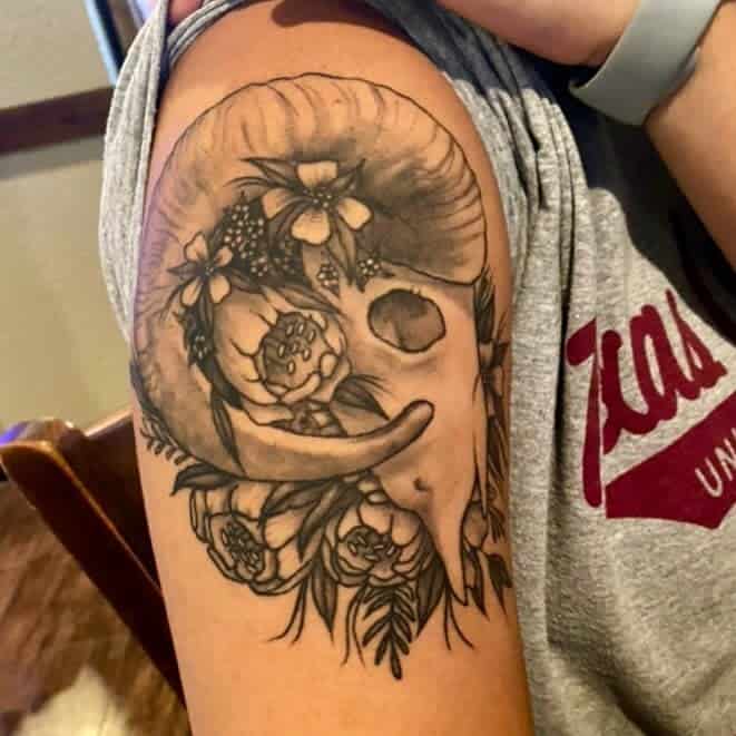 Tattoo of a majestic ram skull adorned with delicate flowers on an upper arm
