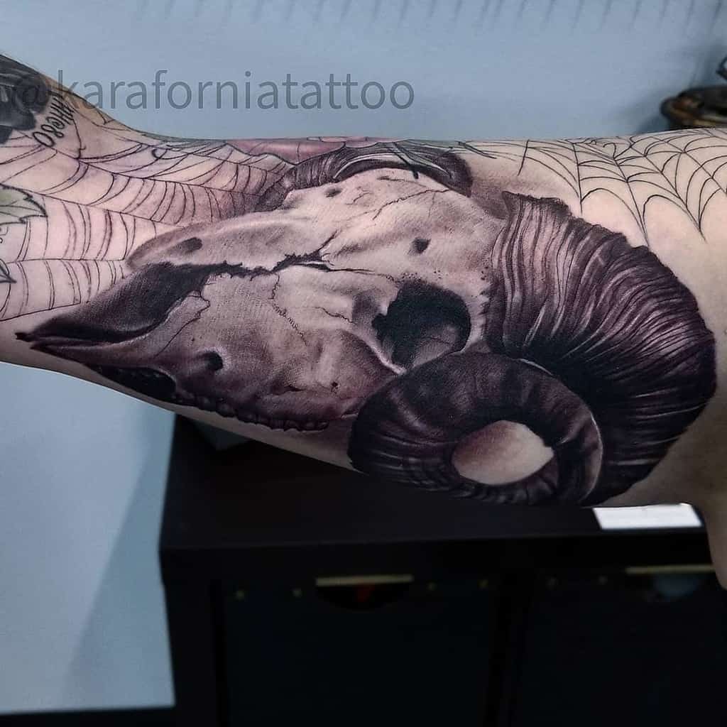 Tattoo of a ram skull with detailed shading and spiderwebs on an upper arm