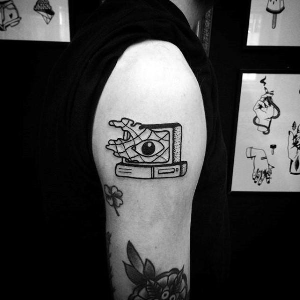 Blackwork tattoo of a vintage computer with a hand reaching out of the screen holding an eye, blending surrealism with tech symbolism.