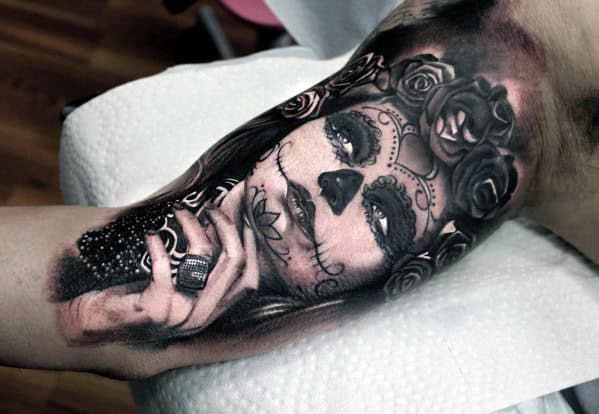 Tattoo of a woman with sugar skull makeup and rose crown on someone's arm