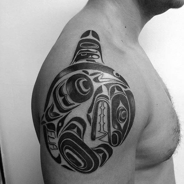 Bold black tribal-style orca tattoo on the upper arm, featuring intricate, flowing patterns and symbolic design elements that form the shape of the whale.