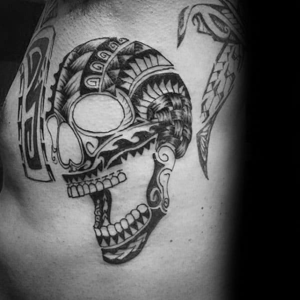 Polynesian-style tribal skull tattoo with intricate geometric patterns and bold black lines, featuring an open jaw and stylized eye.