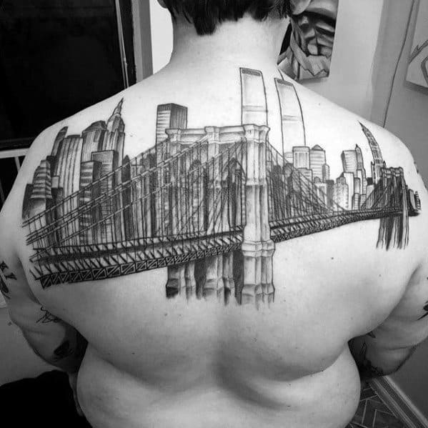 Large black and gray back tattoo of the Brooklyn Bridge stretching across the shoulders, with the New York City skyline in the background.