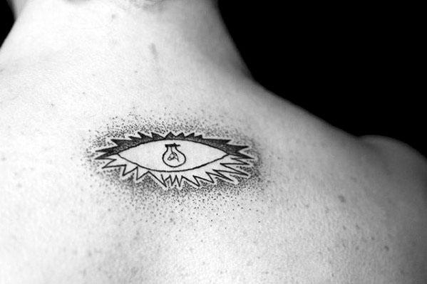 Tattoo of the *Guernica* eye with a light bulb on the upper back, featuring dotwork shading and radiating lines for dramatic effect.
