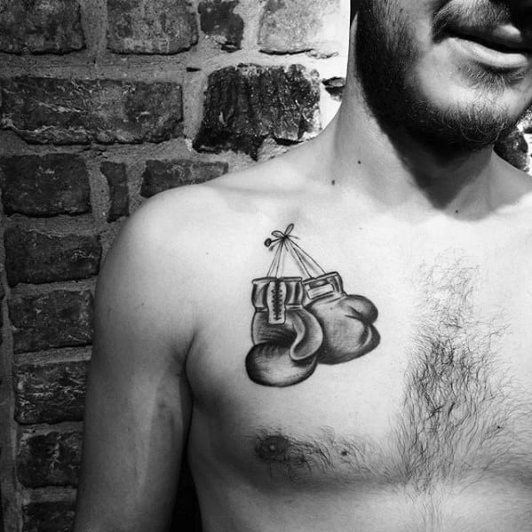 Black and grey chest tattoo of hanging boxing gloves tied by their laces, symbolizing strength and passion for the sport.