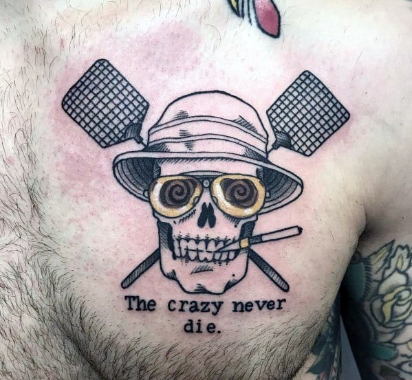 Hunter S. Thompson-inspired tattoo featuring a skull wearing a bucket hat and aviator glasses, with fly swatters crossed behind and the quote "The crazy never die."