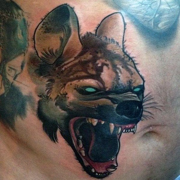 Fierce hyena head tattoo on the chest with glowing green eyes, wide open mouth, sharp fangs, and dark shading for an intense look.