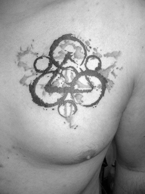 Chest tattoo of the Coheed and Cambria Keywork symbol with a faded, watercolor-inspired effect and soft black ink splashes.