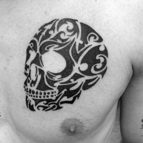 Tribal skull tattoo on the chest with bold black swirls and curved patterns forming a stylized, abstract skull shape.