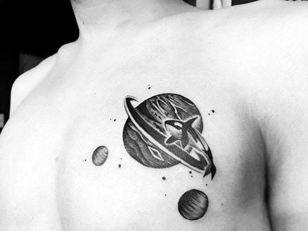 Black and gray tattoo on the chest, featuring a planet with rings and surrounding smaller planets, incorporating intricate shading and dotwork for a cosmic feel.