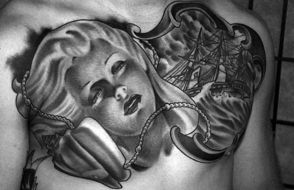 Black and white chest tattoo of a woman's face with a ship and ocean scene