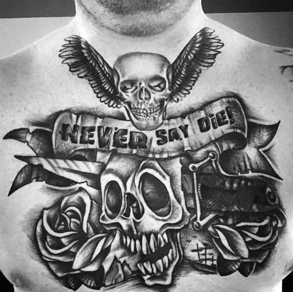 Black and gray chest tattoo featuring a detailed skull, roses, a scroll with "Never Say Die," a winged skull, and pirate-themed elements.
