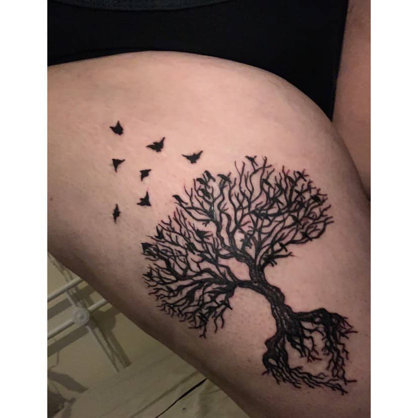 This tattoo features a beautifully intricate tree with exposed roots and branches reaching outward, accompanied by birds flying away—symbolizing growth, transformation, and freedom.