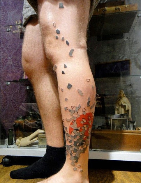 A leg with a tattoo of a 3D effect showing shattered pieces in red and black