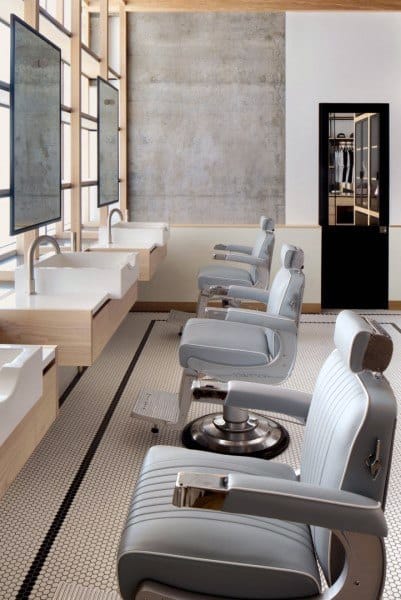 Modern barbershop with sleek gray chairs, tiled flooring, and light wood detailing.