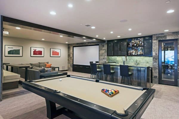Stylish game room with a pool table, bar area, lounge seating, and a projector screen