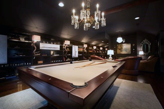 Luxurious billiards room with a chandelier, brown pool table, cozy seating, and stylish decor
