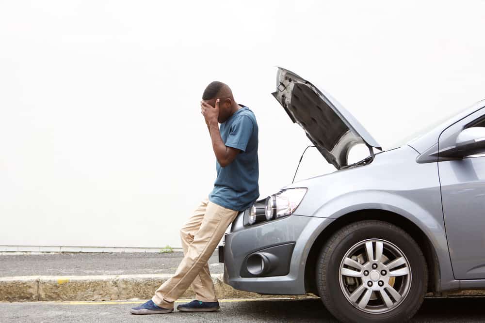 upset young african man standing with his car at road