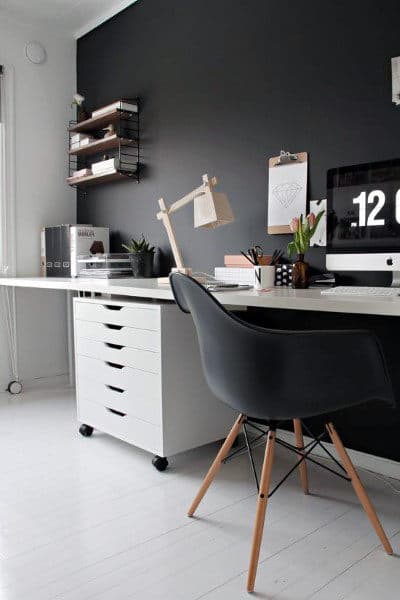 Minimalist home office with a black chair, white desk, computer, and shelves against a black wall