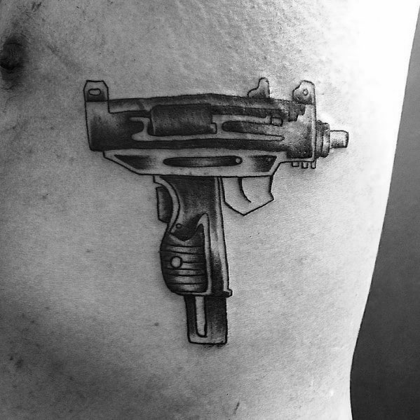 Realistic black and grey Uzi tattoo on the ribcage with fine shading and intricate details, creating a bold and lifelike firearm design.