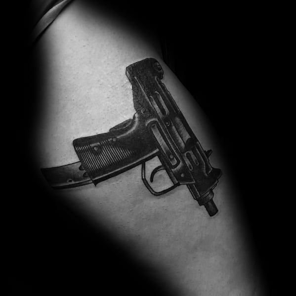 Realistic black and grey Uzi tattoo on the upper arm with detailed shading and a curved magazine, creating a bold and lifelike firearm design.