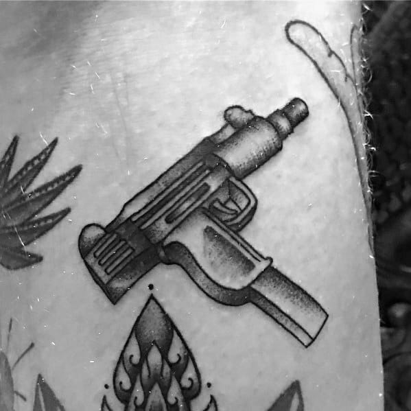 Black and grey Uzi tattoo with bold outlines and shading, featuring a stylized design that blends with surrounding decorative elements.