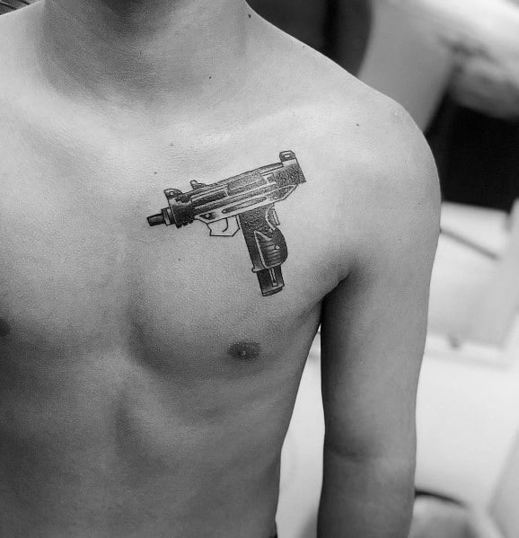 Realistic black and grey Uzi tattoo on the upper chest with fine shading and intricate details, creating a bold and striking firearm design.