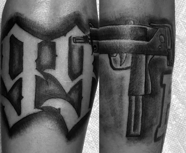 Black and grey Uzi tattoo integrated with bold gothic-style lettering, featuring deep shading and a seamless blend of firearm and typography design.