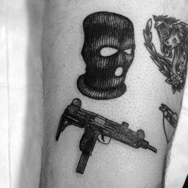 Black and grey Uzi tattoo on the leg, paired with a detailed ski mask design, featuring fine shading and bold contrast for a striking look.