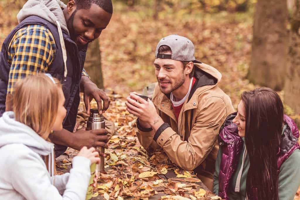 group of friends drinking hot water from a thermos at a picnic bench in autumn