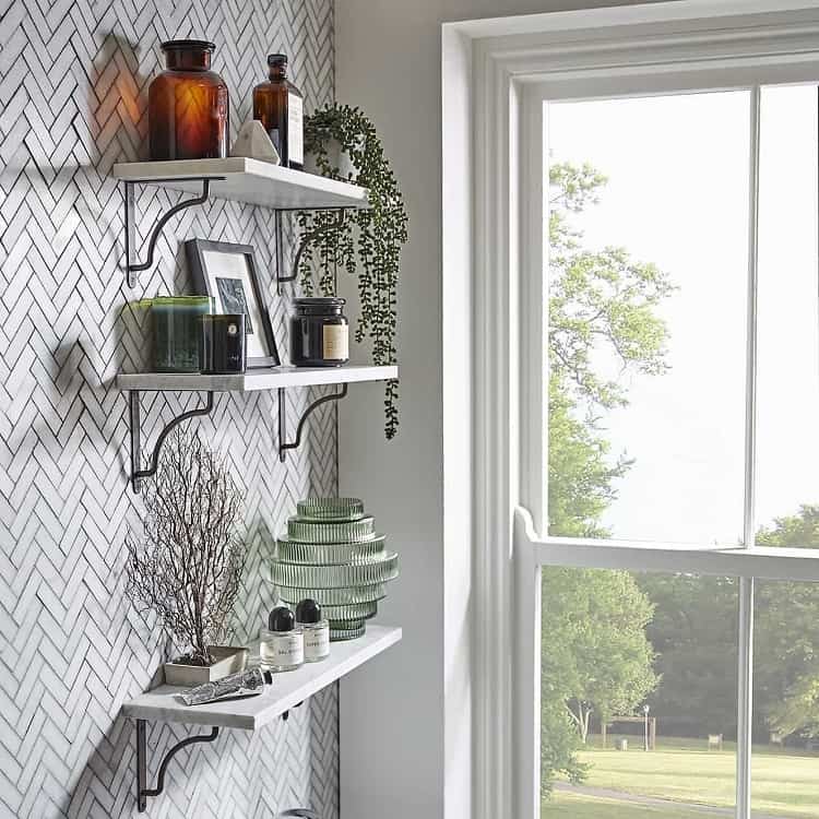 White bathroom shelves with decor items, glass bottles, and a large window view.