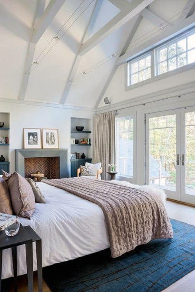 Bright bedroom with vaulted ceiling, fireplace, and French doors leading to an outdoor view.