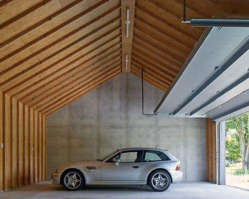 Minimalist garage with vaulted wooden ceiling and a sleek silver car.