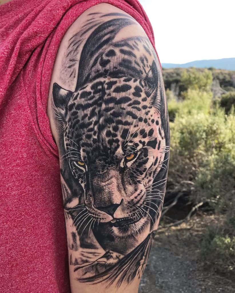 A striking black and grey tattoo of a jaguar's intense gaze and detailed face, wrapping around the upper arm with realistic shading.