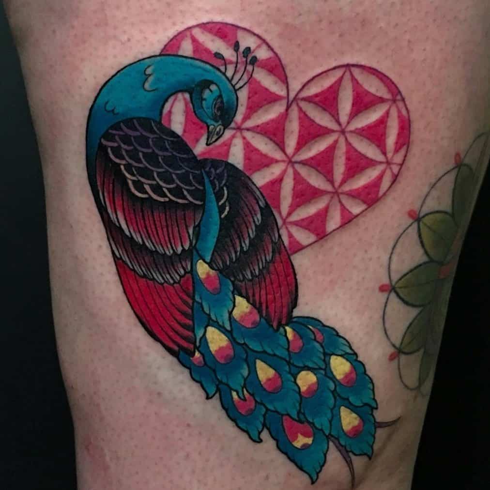 Peacock tattoo with colorful feathers in blue, green, and red, with geometric heart shapes in the background.