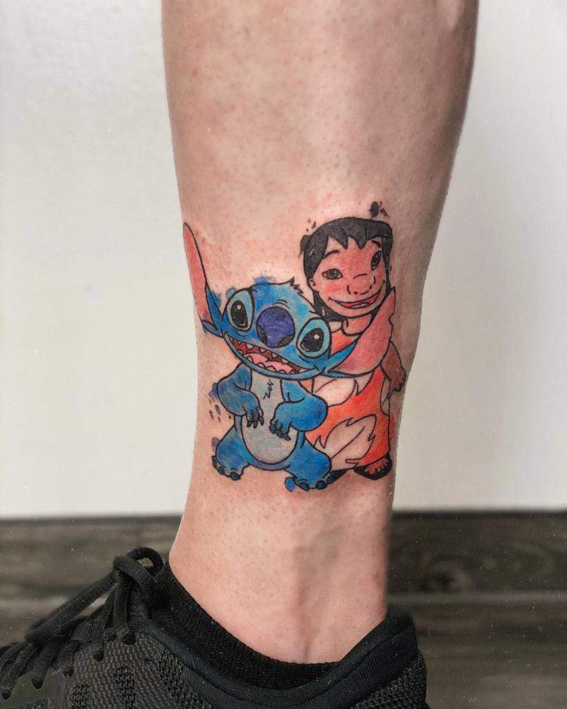 Colorful tattoo of Stitch from Lilo & Stitch with Lilo, both smiling and posing together, on the lower leg.