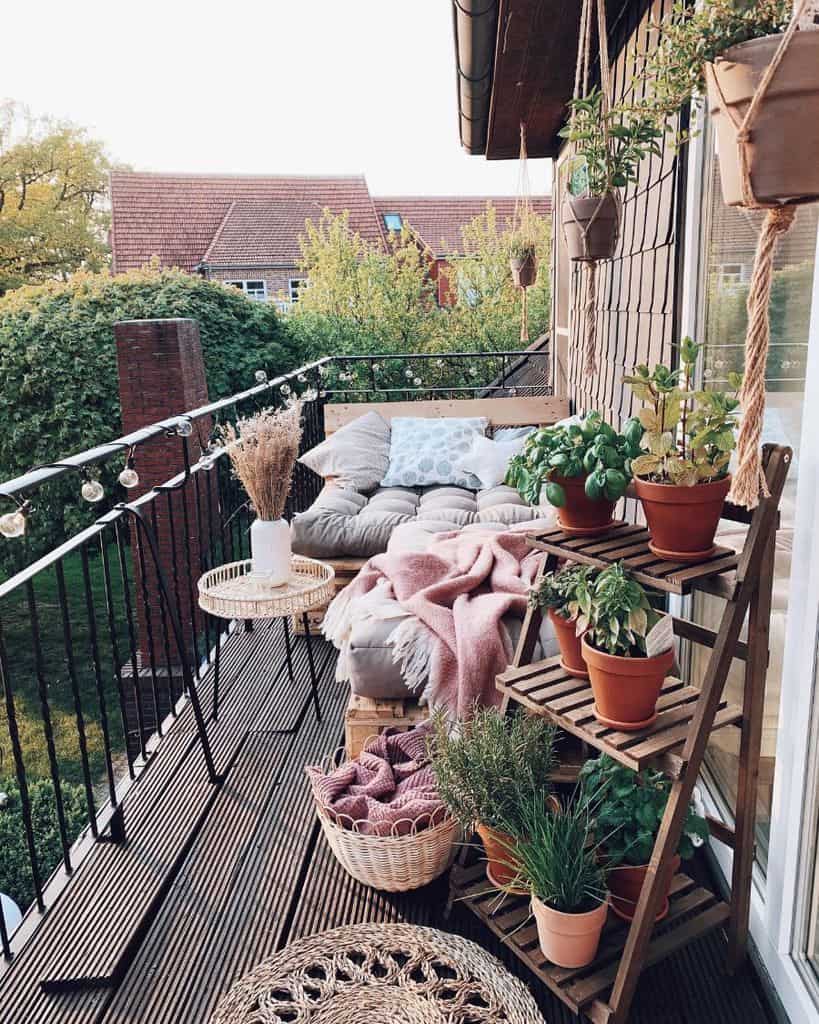 Cozy balcony with potted herbs, hanging plants, a cushioned couch, and wooden decor.