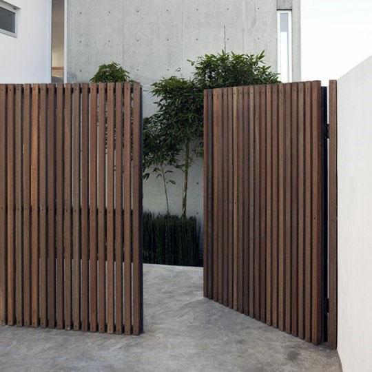 Wooden slat gates partially open, revealing a modern concrete building and greenery behind