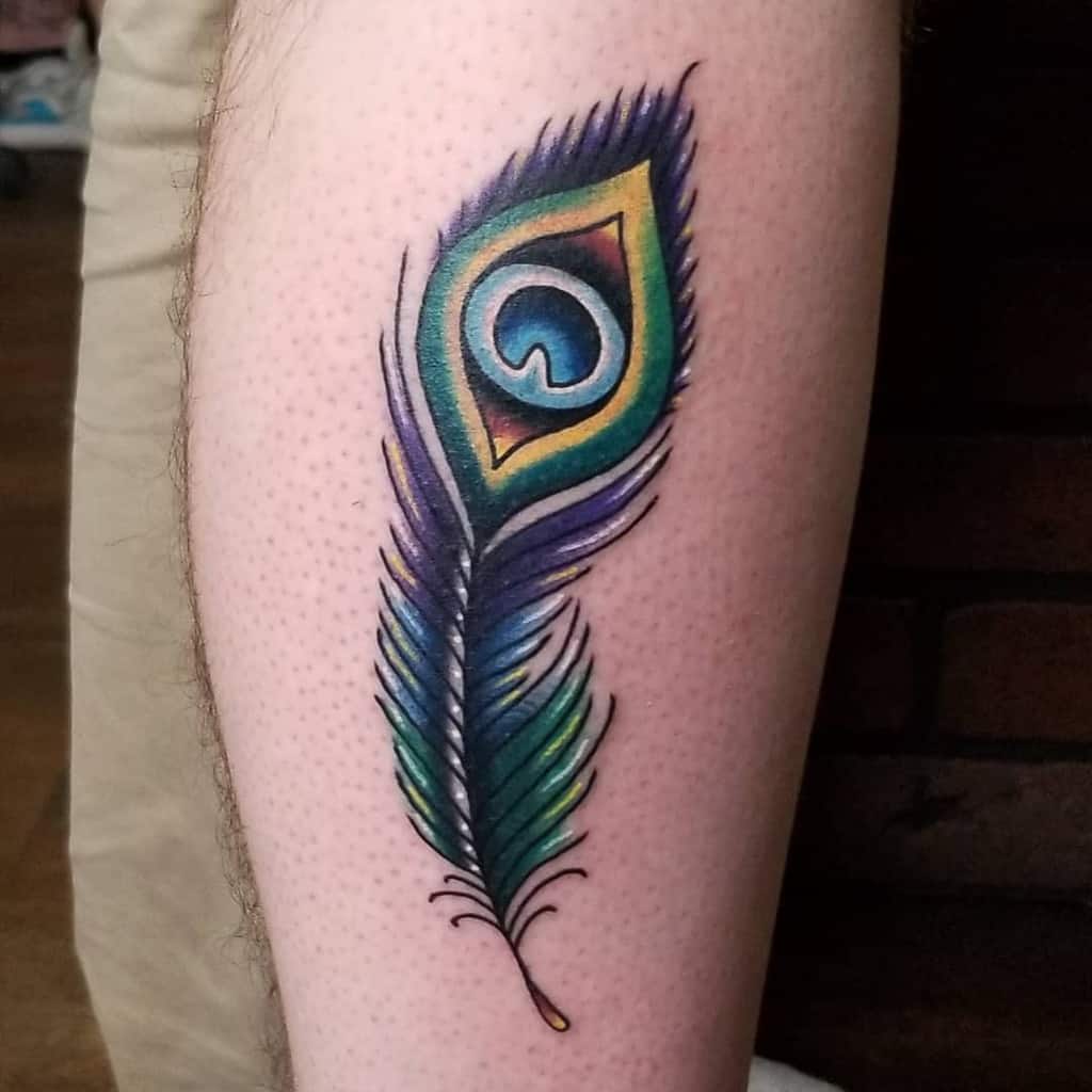 Colorful peacock feather tattoo on the leg, featuring rich blue, green, and gold hues with bold outlines and smooth shading.