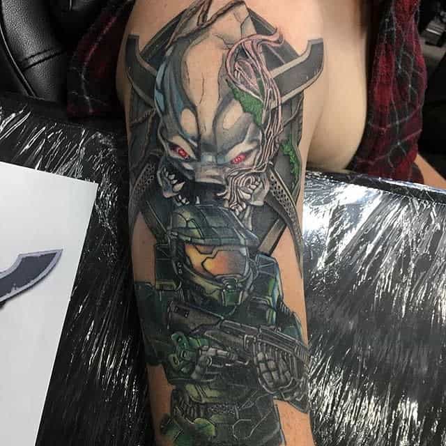 Detailed Halo tattoo featuring Master Chief with a battle rifle and a menacing Sangheili Elite above, glowing red eyes and biomechanical details.