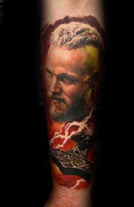Tattoo of a bearded man with white hair and a pendant on a forearm against a fiery background