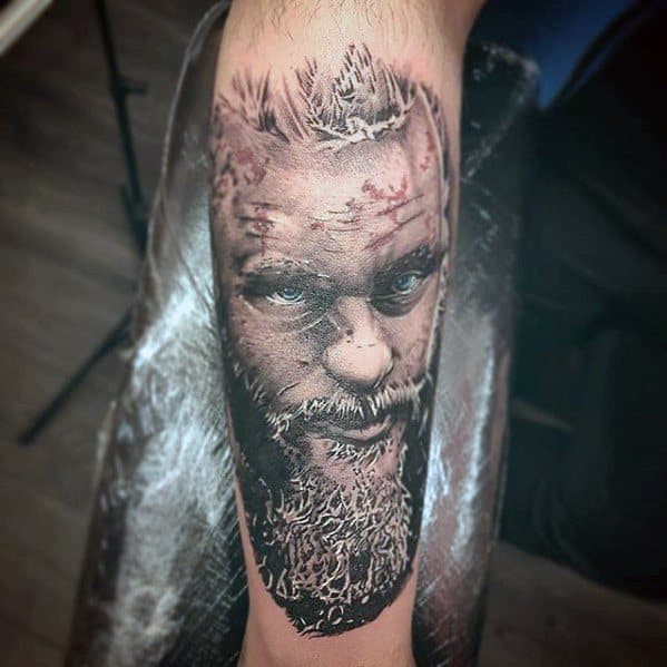 Realistic tattoo of a bearded man's face on a person's arm